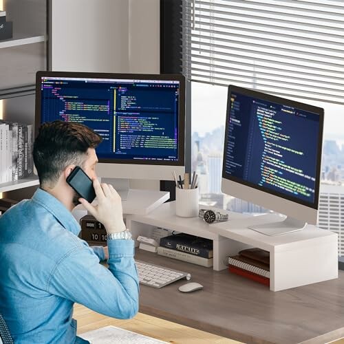 Person talking on phone at desk with dual monitors displaying code.